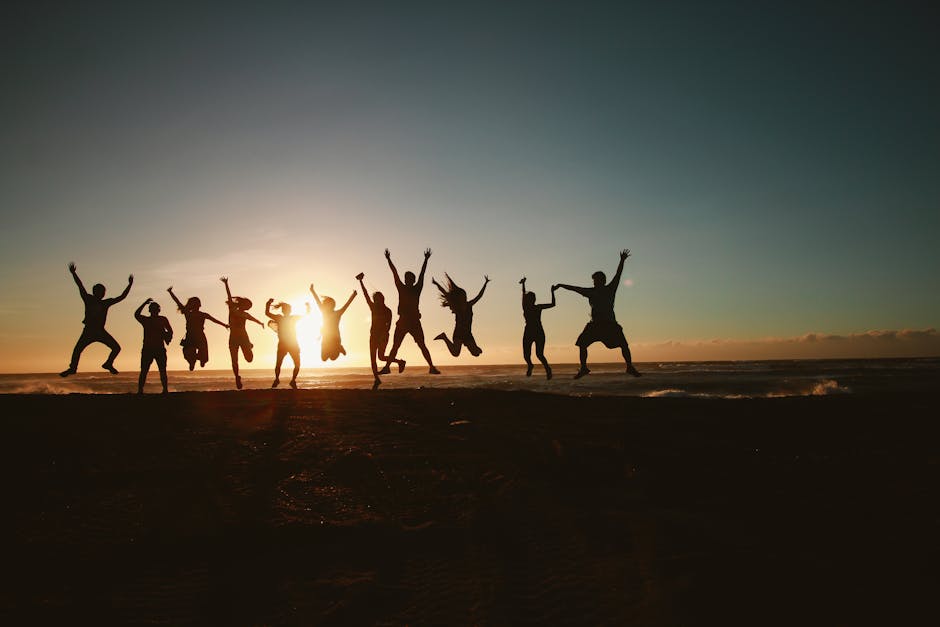 Silhouette of a group of friends jumping on a beach at sunset, expressing joy and freedom